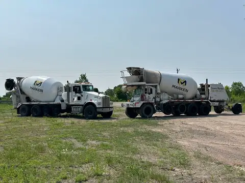 Two concrete mixer trucks parked on a gravel site in Gilman, MN