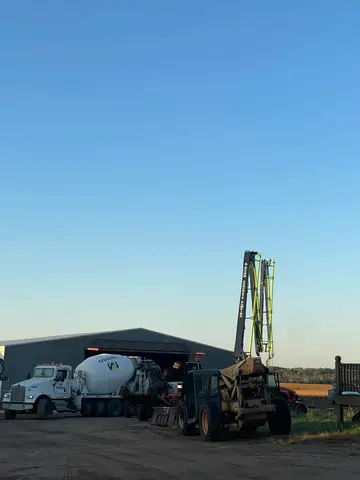 Concrete mixer truck and equipment parked near a large shed