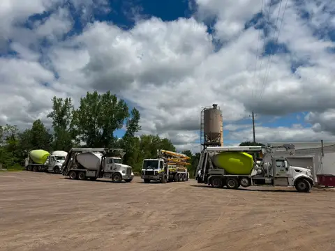 Multiple concrete trucks lined up at a construction site under clouds