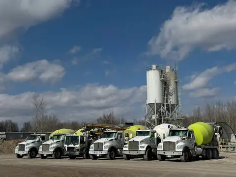 Five concrete mixer trucks parked near a cement silo in Gilman
